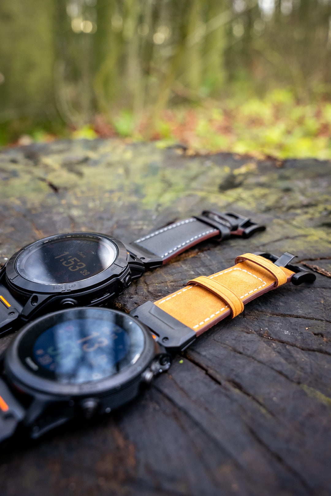 Two watches with leather straps on a wooden surface with a blurred natural background
