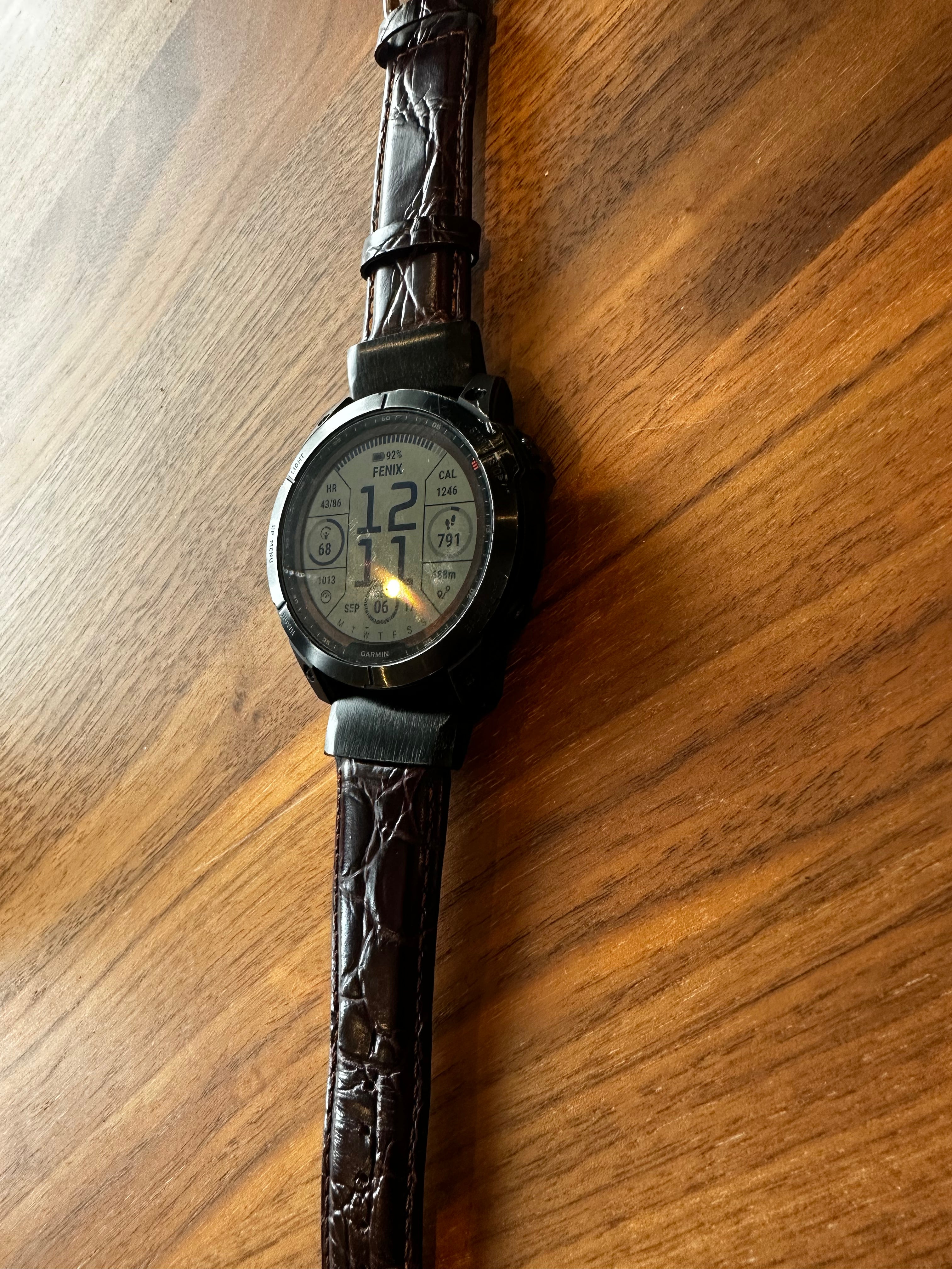 Garmin Fenix 7X with a brown leather strap on a wooden surface